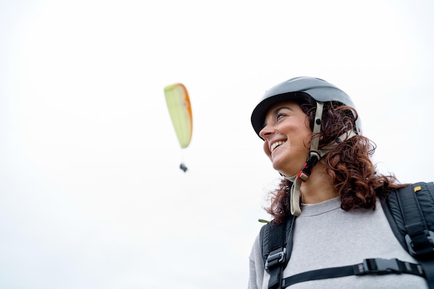 Side view of cheerful woman with helmet and paragliding equipment outdoors. Panoramic view of adventurous woman practicing risky sports. Adventure and sport lifestyle.