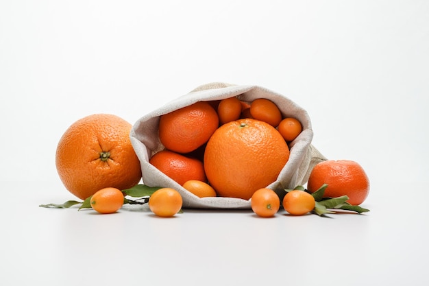 Side view of citrus fruits as orange kumquat tangerine in sack and on white background