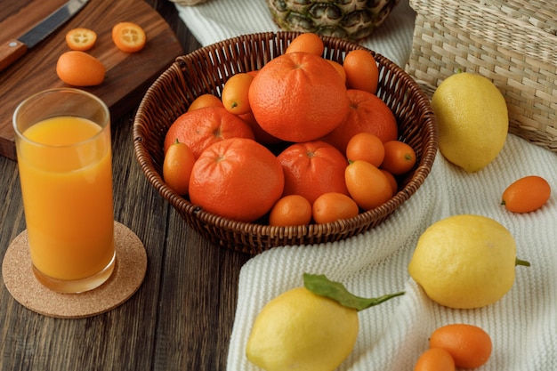 Side view of citrus fruits as tangerine kumquat in basket lemons on cloth with orange juice on wooden background