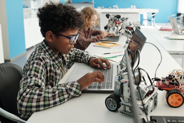 Side view of clever african american schoolboy sitting in front of laptop