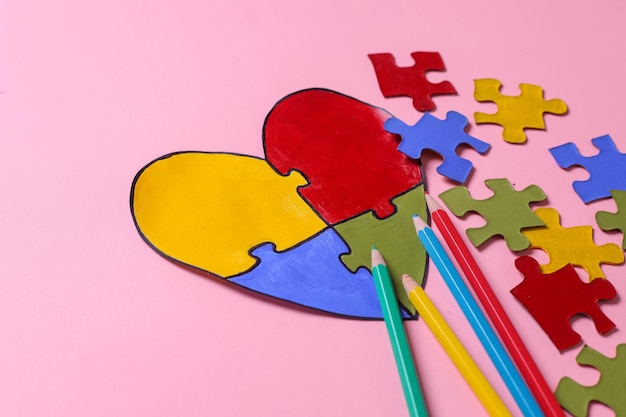 Side view of colorful puzzle heart shape pieces of colorful puzzles and pencils on pink background