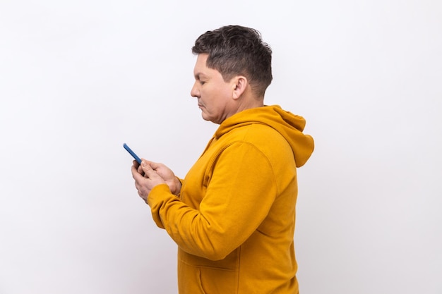 Side view of concentrated middle aged man texting message in social media on cell phone