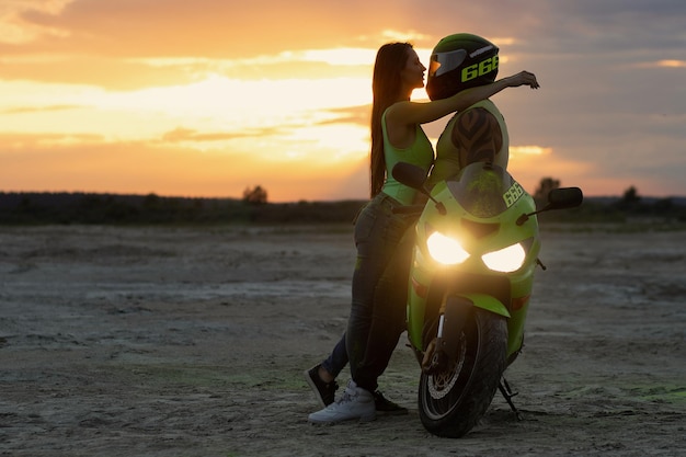 Side view of couple in love tenderly hugging near motorcycle parked on sandy seashore