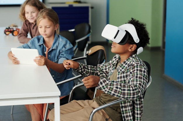 Side view of cute african american schoolboy in vr headset controling robot