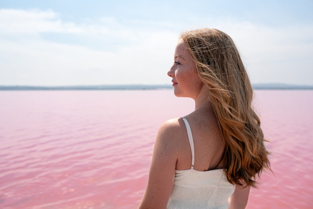 Side view of cute teenager woman wearing summer clothes standing on an amazing pink lake