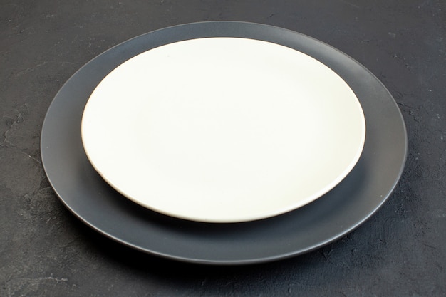 Side view of dark color and white empty plates in different sizes on black background