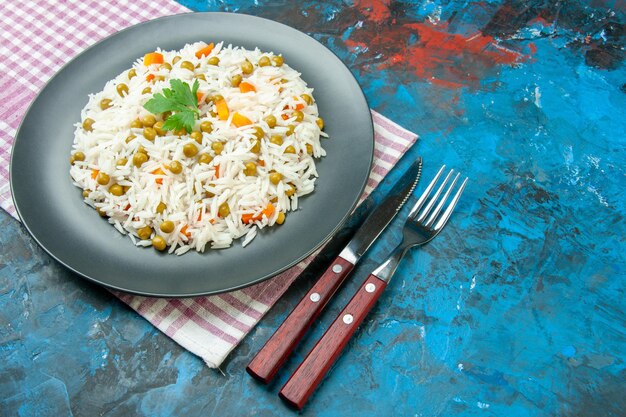 Photo side view of delicious rice meal with pisum carrot on purple towel and cutlery set on blue background