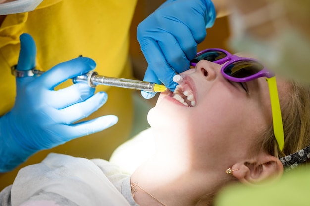 Side view of dentist holding a syringe and anesthetizing her little girl patient Doctors dentists giving for child an injection anesthesia Stomatology for kids conceptcomfortable dental treatment