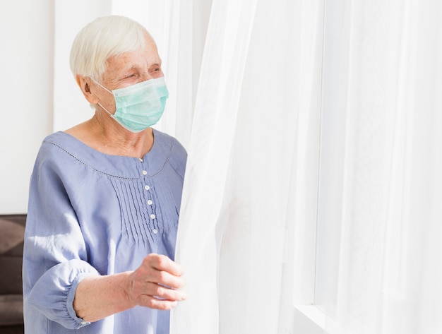 Side view of elder woman with medical mask looking through the window