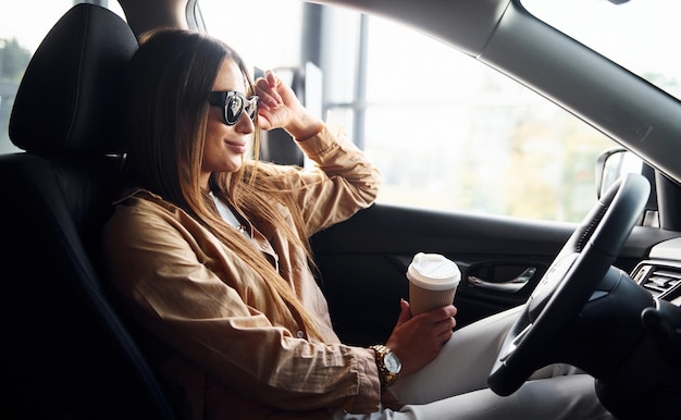 Side view of fashionable beautiful young woman that is inside her modern automobile