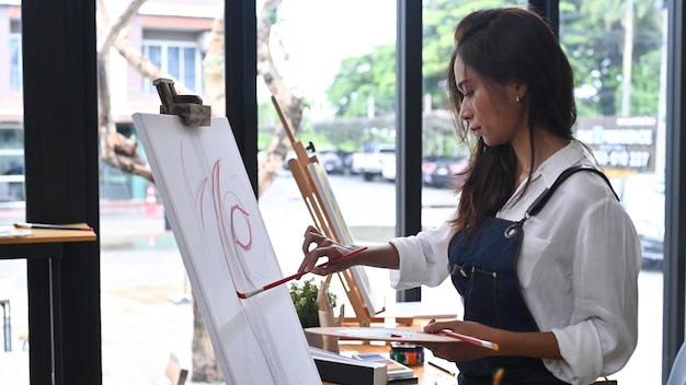 Side view female artist painting with watercolor on easel in art studio