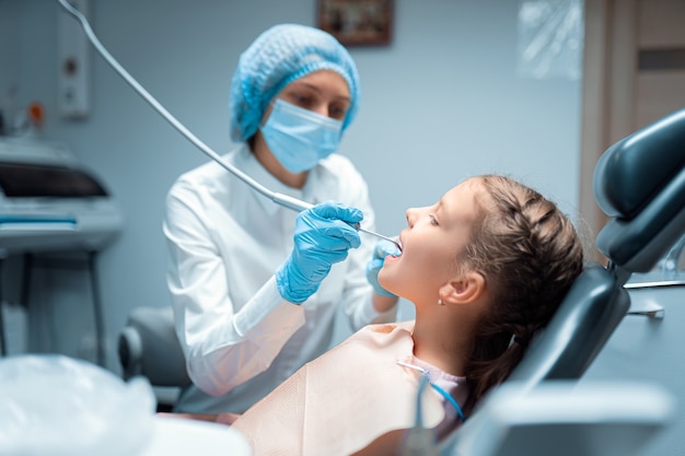 Photo side view of female dentist who treats teeth of little child patient in dental office dentistry