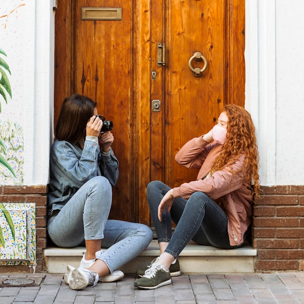 Side view of female friends with face masks taking pictures with camera