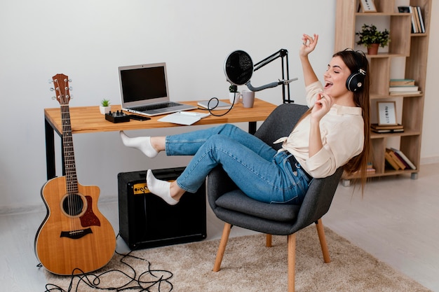 Side view of female musician at home singing with headphones on next to acoustic guitar