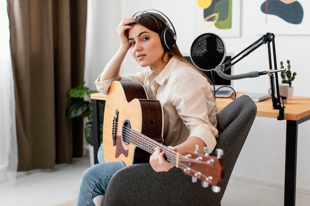 Side view of female musician posing with acoustic guitar at home