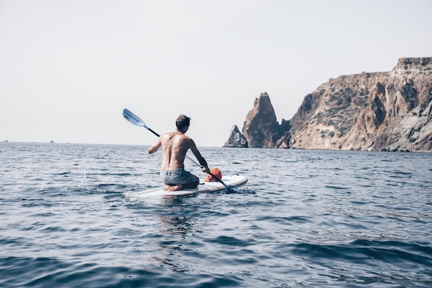 Side view foto of a man swiming and relaxing on the sup board sportive man in the sea on the stand