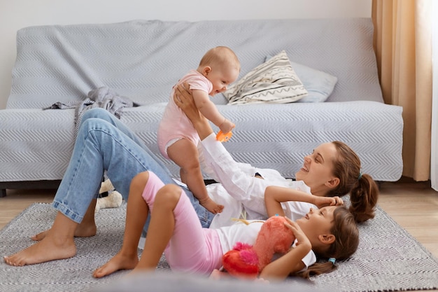 Side view full length portrait of smiling woman holding baby daughter in hands while lying on floor mother playing with her children enjoying to spend time together