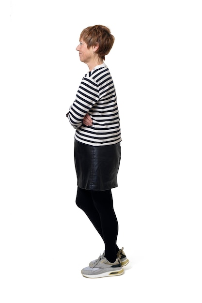 Side view full length portrait of a woman in skirt striped sweater and sneakers with arms crossed on white background