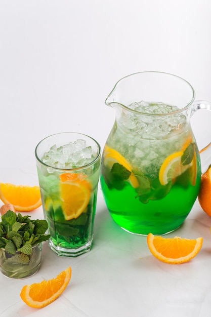 Side view on green lemonade in a jug and glass on the white background