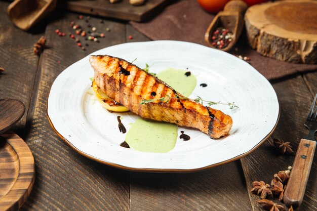 Side view on grilled salmon steak in green sauce on the wooden decorated table