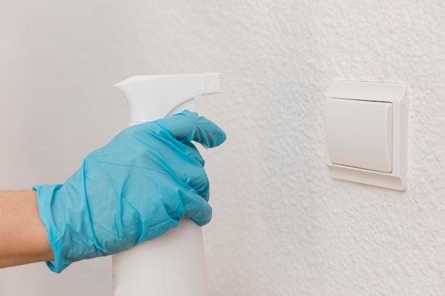 Side view of hand with surgical glove spraying disinfectant on light switch