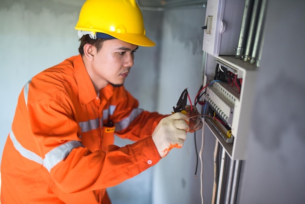 Side view of a handsome Asian electrician repairing an electrical box with pliers in the corridor