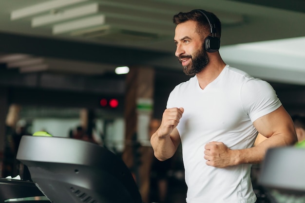 Side view of a handsome athlete running on a treadmill in the gym The guy is wearing a white shirt