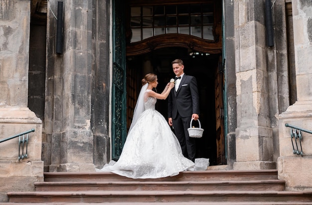 Side view of handsome bridegroom in stylish suit holding basket and waiting for his bride which tying buttonhole to another side of his jacket after wedding ceremony in ancient church