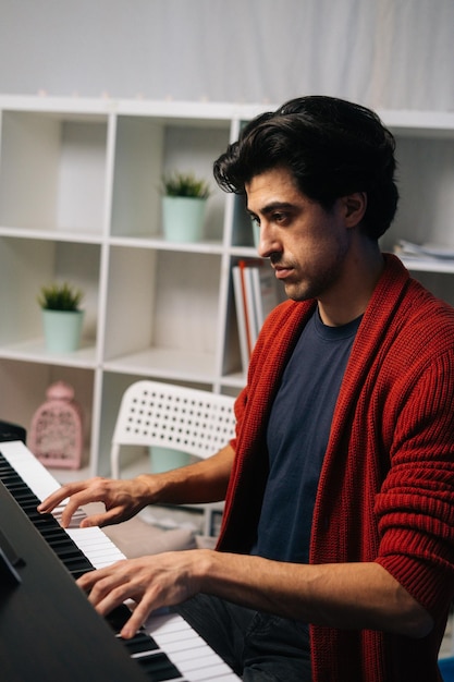 Side view of handsome young musician man playing piano at home studio during lesson in free time