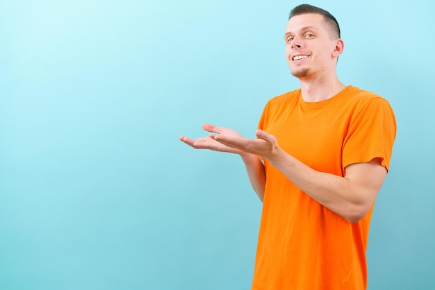 A side view of a happy white man in an orange tshirt pointed both hands on the upper side Showing empty copy space on blue background Handsome Joyful Model Present Product Confidence