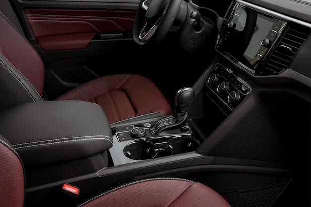 Side view of the interior of a luxurious car dashboard, red leather seats, automatic transmission, steering wheel and touch screen