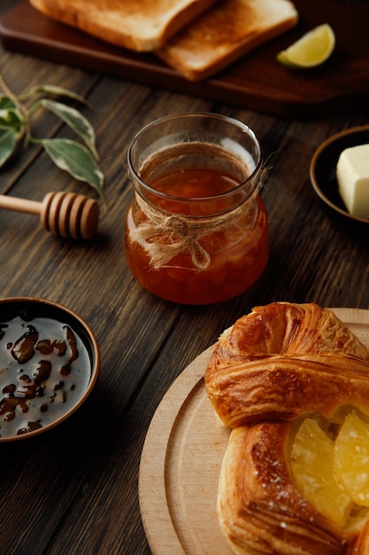 Side view of jar of quince jam with dried bread slices and lime slice croissant butter on wooden background