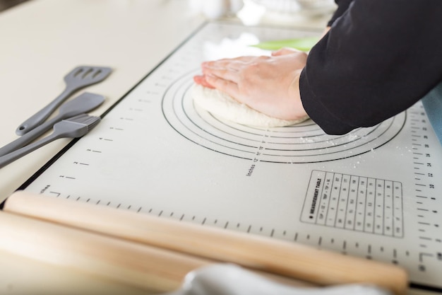 Side view of kneading dough on rubber kitchen mat on white kitchen table