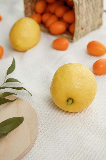 Side view of lemons with kumquats spilling out of basket on white cloth background