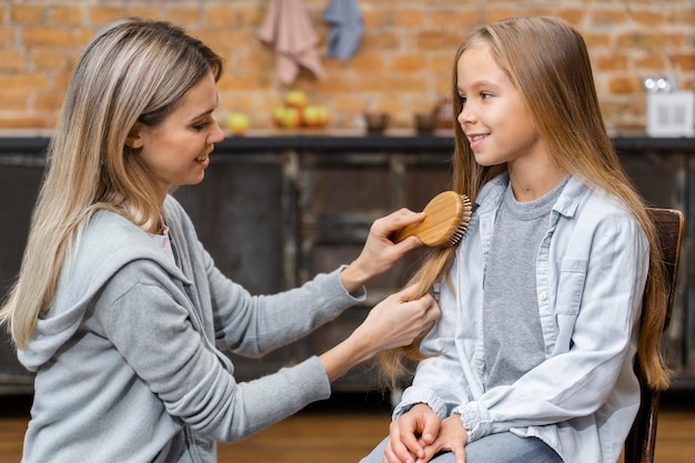 Side view of little girl getting her hair brushed by hairdresser