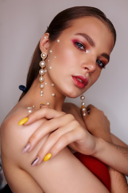 Side view of lovely woman in pearl earrings and with fashionable makeup looking at camera