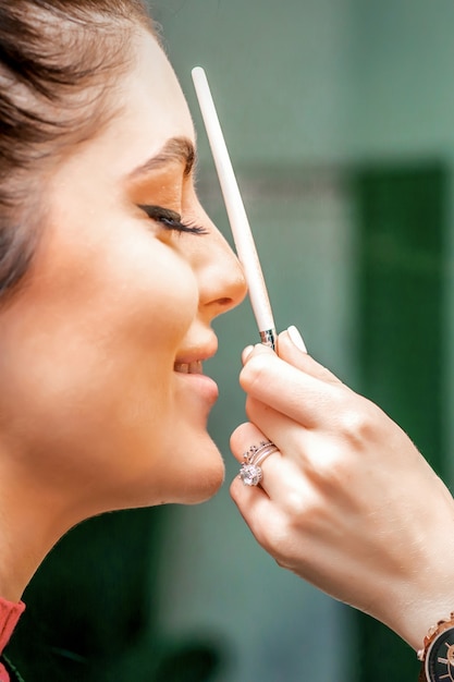 Side view of a makeup artist using aerograph making an airbrush makeup foundation on a female face