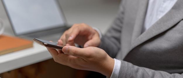 Side view of male entrepreneur hands using smartphone while sitting at white office desk