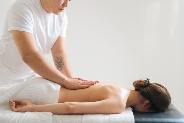 Side view of male masseur massaging back of young female lying on massage table on white background