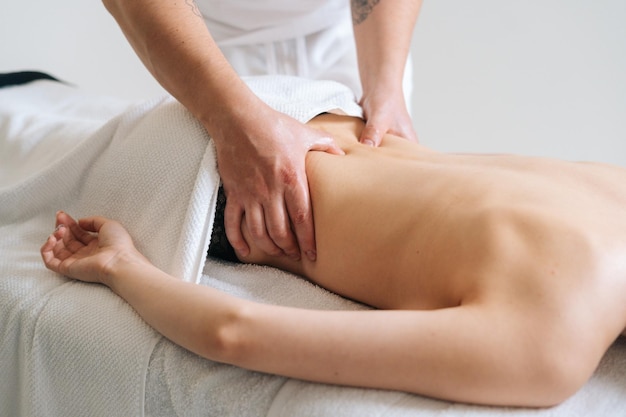 Side view of male masseur massaging lower back of woman lying on massage table on white background