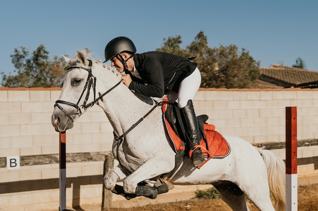 Side view of a male rider jumping over obstacles with his white horse