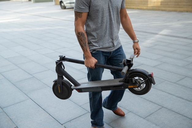 Side view man carrying electric scooter