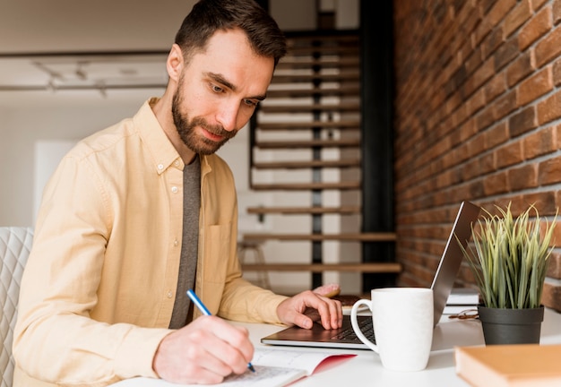 Side view man having video call on laptop and writing