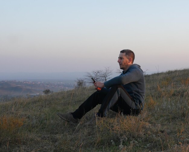 Photo side view of man sitting on hill against sky