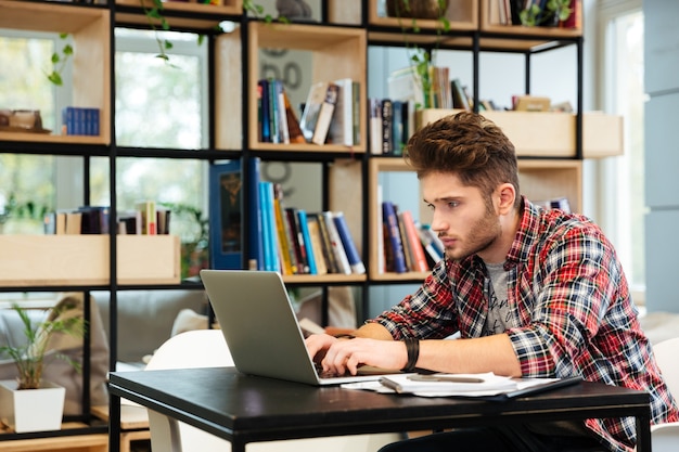 Side view of man sitting at the table and writing something on laptop in office.