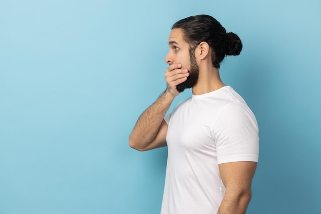 Side view of man with beard wearing white Tshirt covering mouth doesnt want to spread rumours