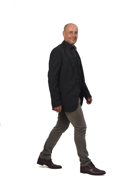 Side view of a man with blazer and jeans walking and looking at camera on white background