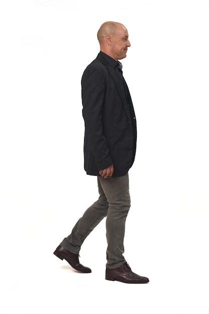 Side view of a man with blazer and jeans walking on white background