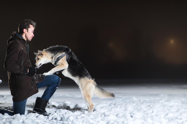 Side view at a man with mixed breed dog outside at night in winter