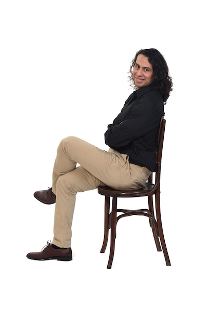 side view of a man with shirt, shoes and pants  sitting on chair arms and legs crossed and looking at camera on white background